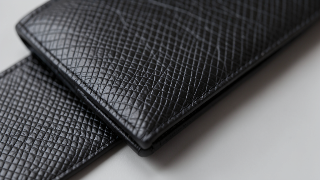 Cuir saffiano : ce que le gaufrage change vraiment 1 Cuir saffiano noir d'un portefeuille homme, rayures croisees vues de pres