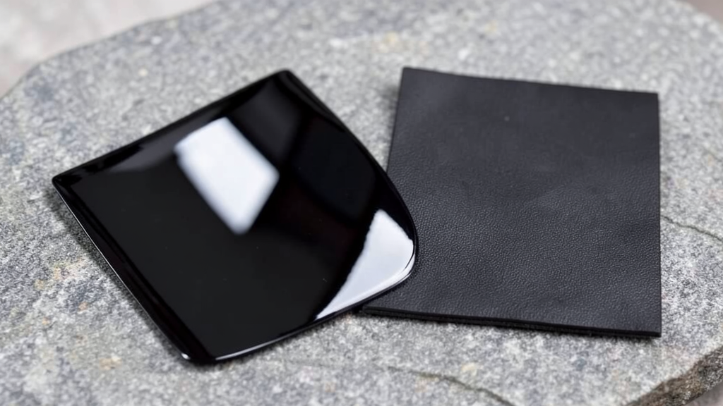 Cuir verni : fabrication, qualités et limites 1 Échantillon de cuir verni noir brillant posé à côté d'un cuir noir mat sur une pierre grise