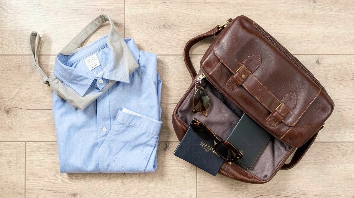 Que mettre dans son sac de voyage ? : check-list 3 Packliste Urlaub: gefaltetes Hemd, Reisepass und Sonnenbrille neben einer braunen Reisetasche aus Leder